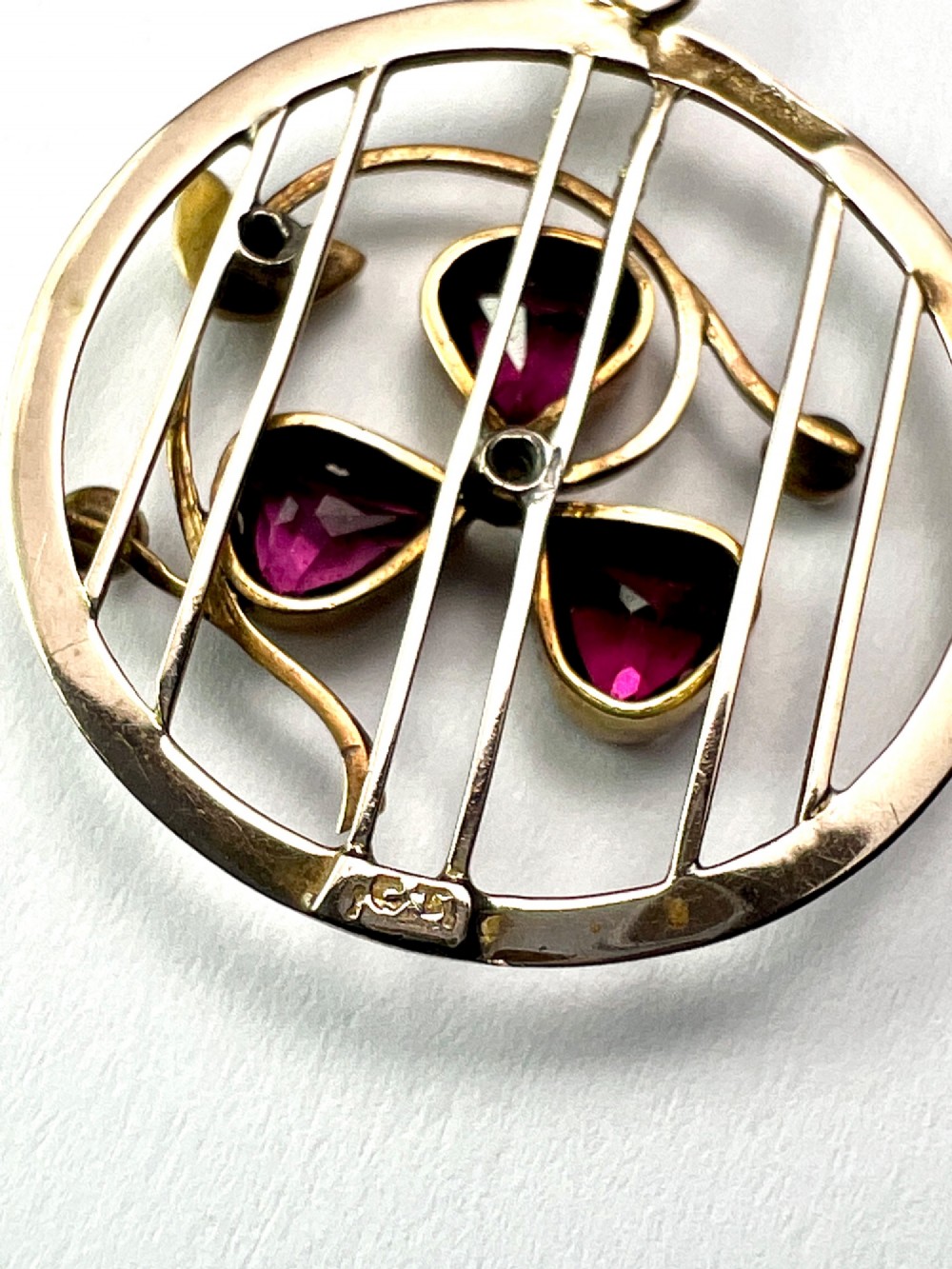 A circular 9ct gold Edwardian openwork pendant featuring three heart-cut deep red garnets forming a clover motif flanked by seed pearls. View V