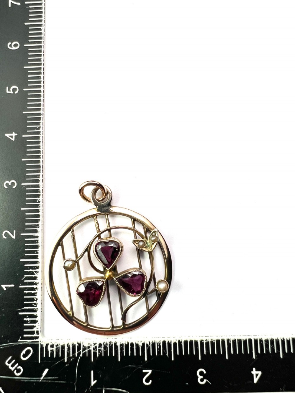 A circular 9ct gold Edwardian openwork pendant featuring three heart-cut deep red garnets forming a clover motif flanked by seed pearls. View VII