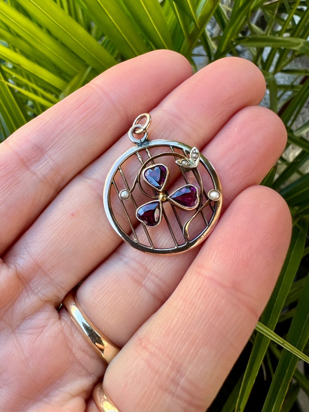 A circular 9ct gold Edwardian openwork pendant featuring three heart-cut deep red garnets forming a clover motif flanked by seed pearls. View VIII