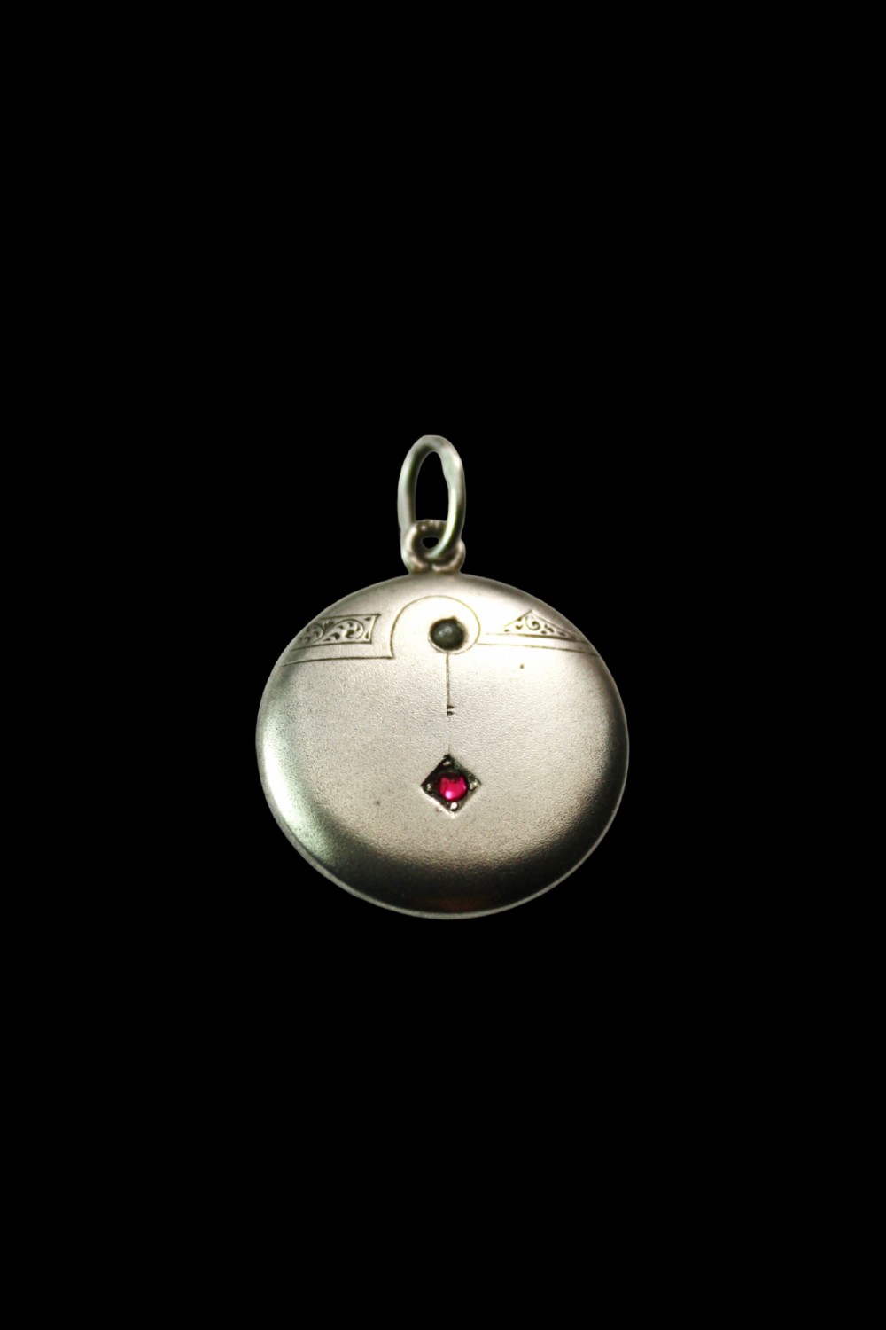 A circular silver Art Nouveau pendant featuring engraved line details, a central seed pearl, and a flush-set red paste stone. View III
