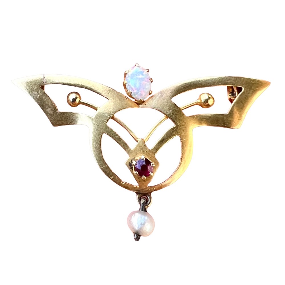 An Art Nouveau 18ct gold openwork brooch featuring a claw-set central opal, a red ruby, and a dangling pearl drop.