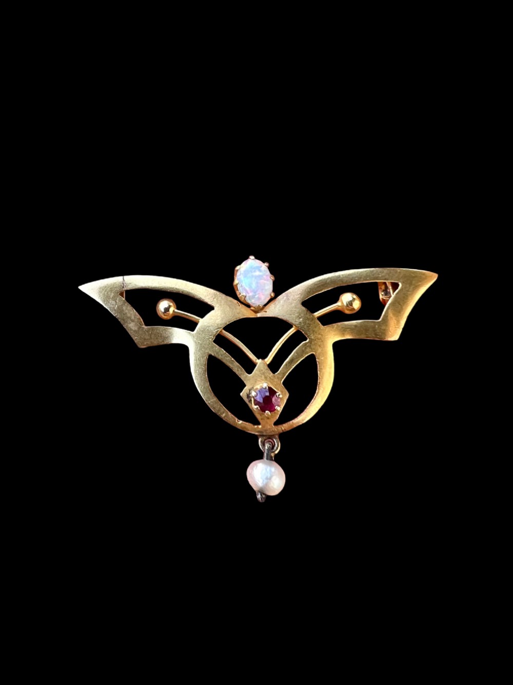 An Art Nouveau 18ct gold openwork brooch featuring a claw-set central opal, a red ruby, and a dangling pearl drop. View II