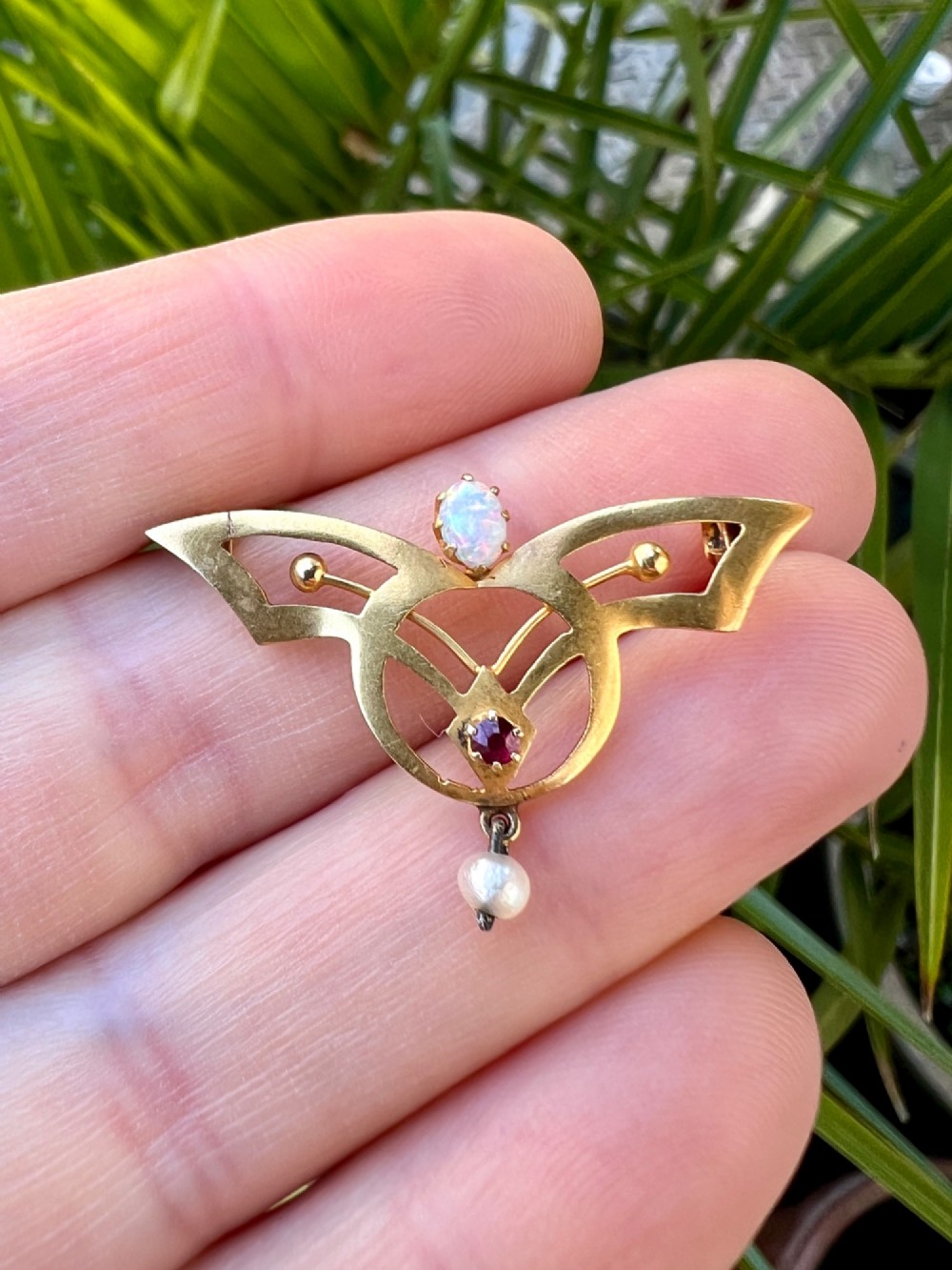 An Art Nouveau 18ct gold openwork brooch featuring a claw-set central opal, a red ruby, and a dangling pearl drop. View IV