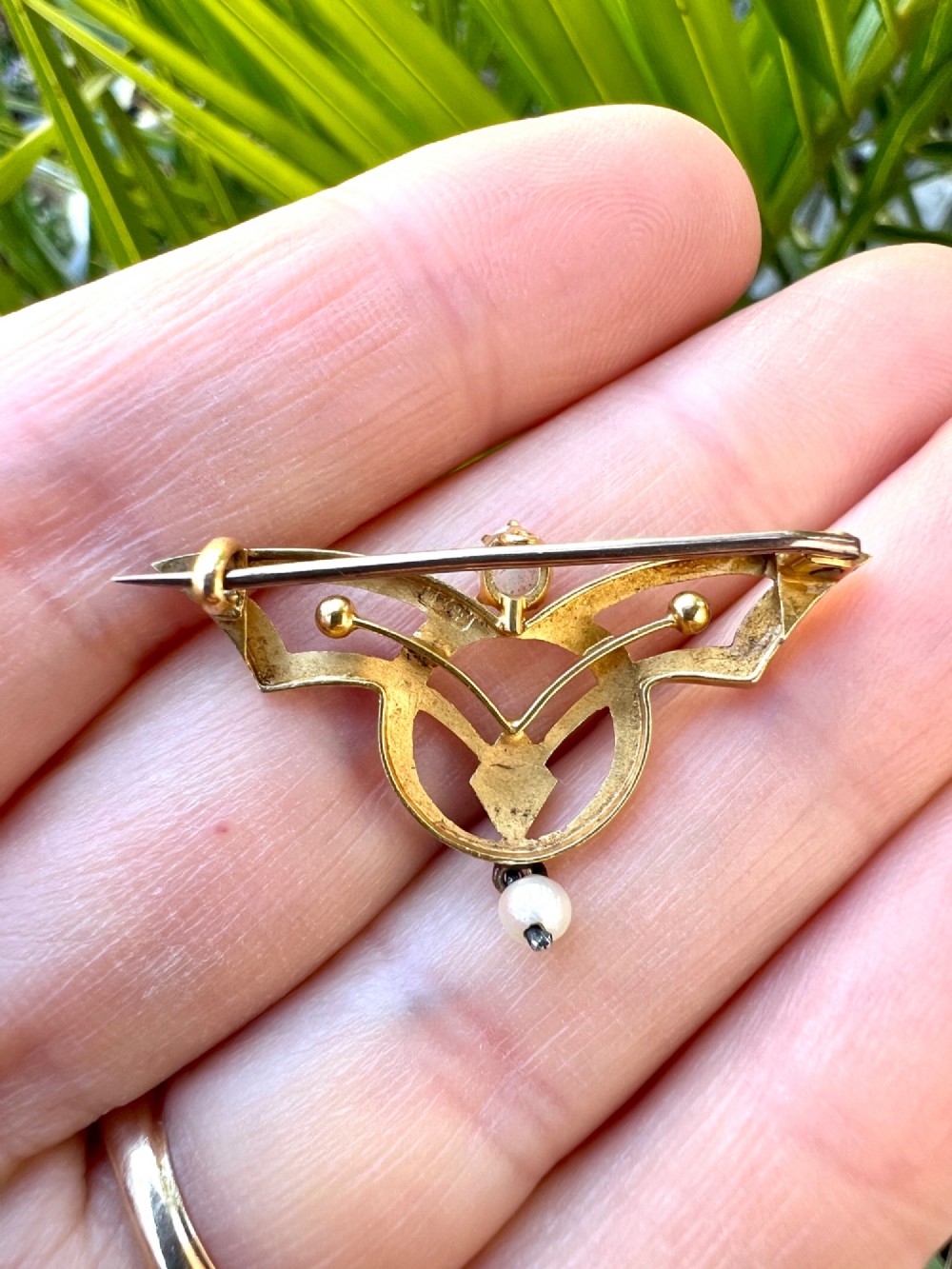 An Art Nouveau 18ct gold openwork brooch featuring a claw-set central opal, a red ruby, and a dangling pearl drop. View V
