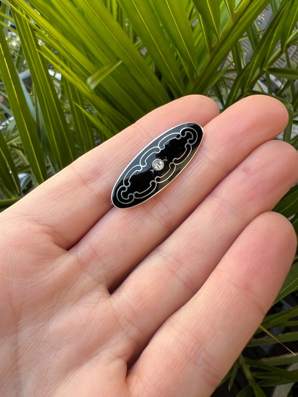 An oval Art Deco brooch featuring black enamel inlay with silver scroll linework and a central clear glass paste stone. View IV
