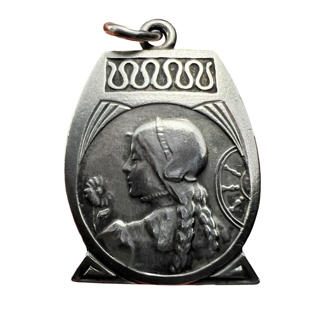 An antique French Art Nouveau silver medallion pendant featuring a relief carving of a woman in profile holding a flower beside a spinning wheel.