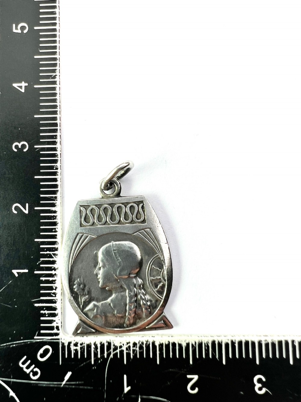 An antique French Art Nouveau silver medallion pendant featuring a relief carving of a woman in profile holding a flower beside a spinning wheel. View IV