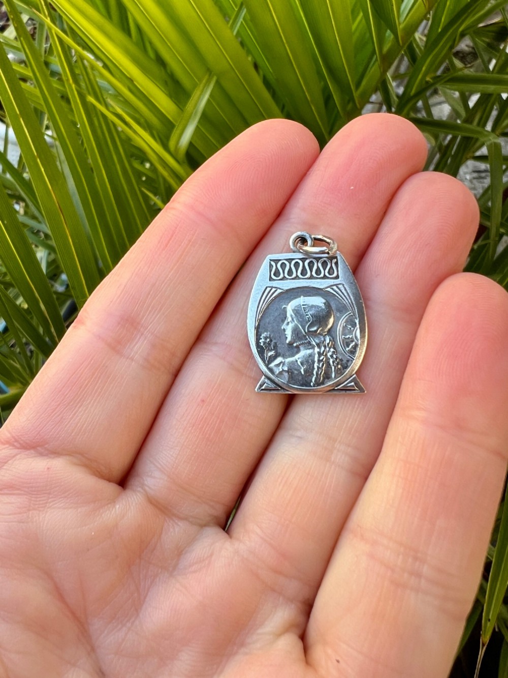 An antique French Art Nouveau silver medallion pendant featuring a relief carving of a woman in profile holding a flower beside a spinning wheel. View V