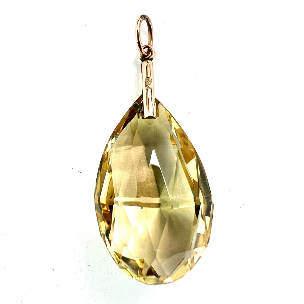 A faceted teardrop-cut yellow citrine gemstone attached to a simple 9ct gold bail stamped with hallmarks.