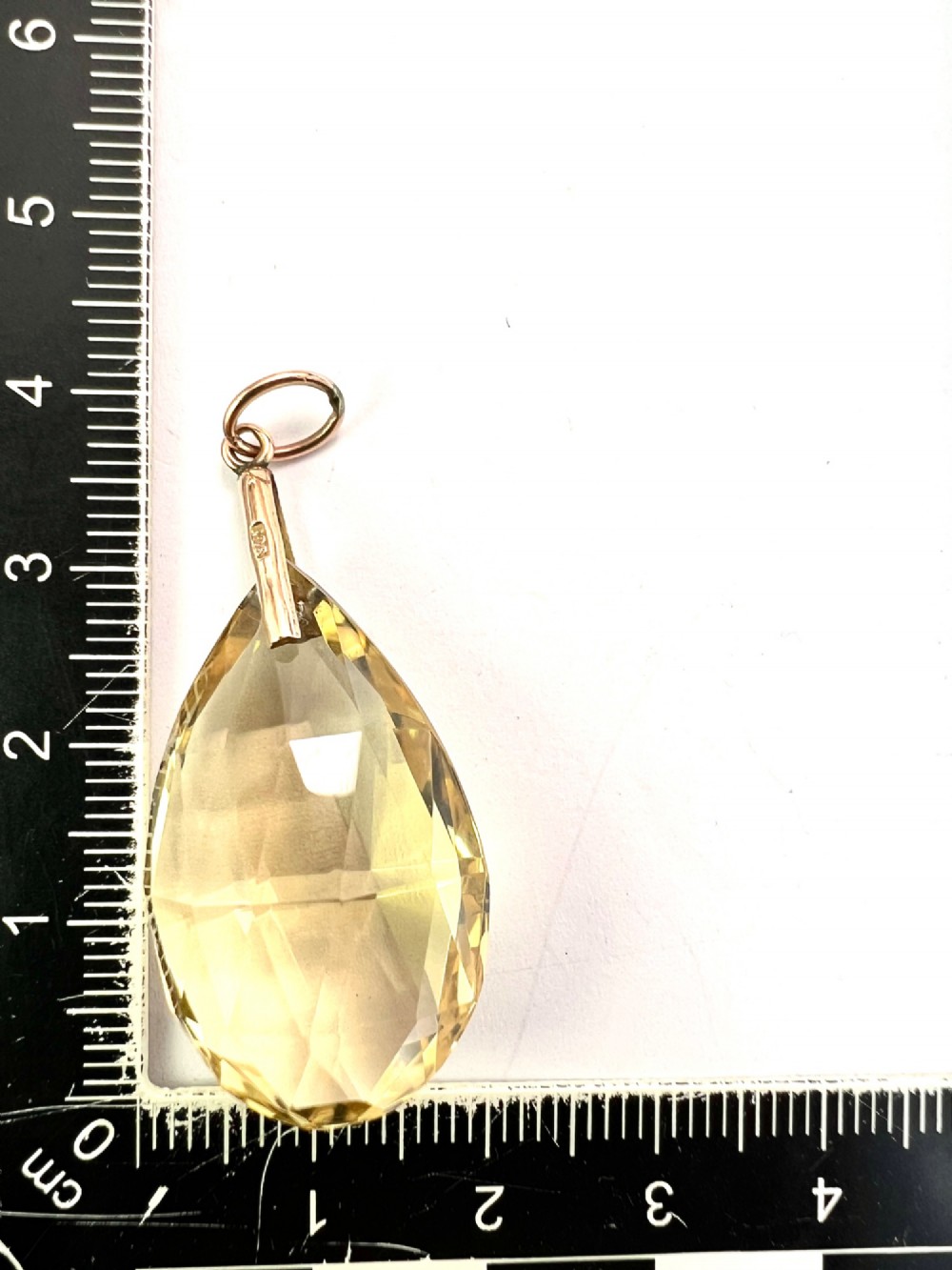 A faceted teardrop-cut yellow citrine gemstone attached to a simple 9ct gold bail stamped with hallmarks. View V