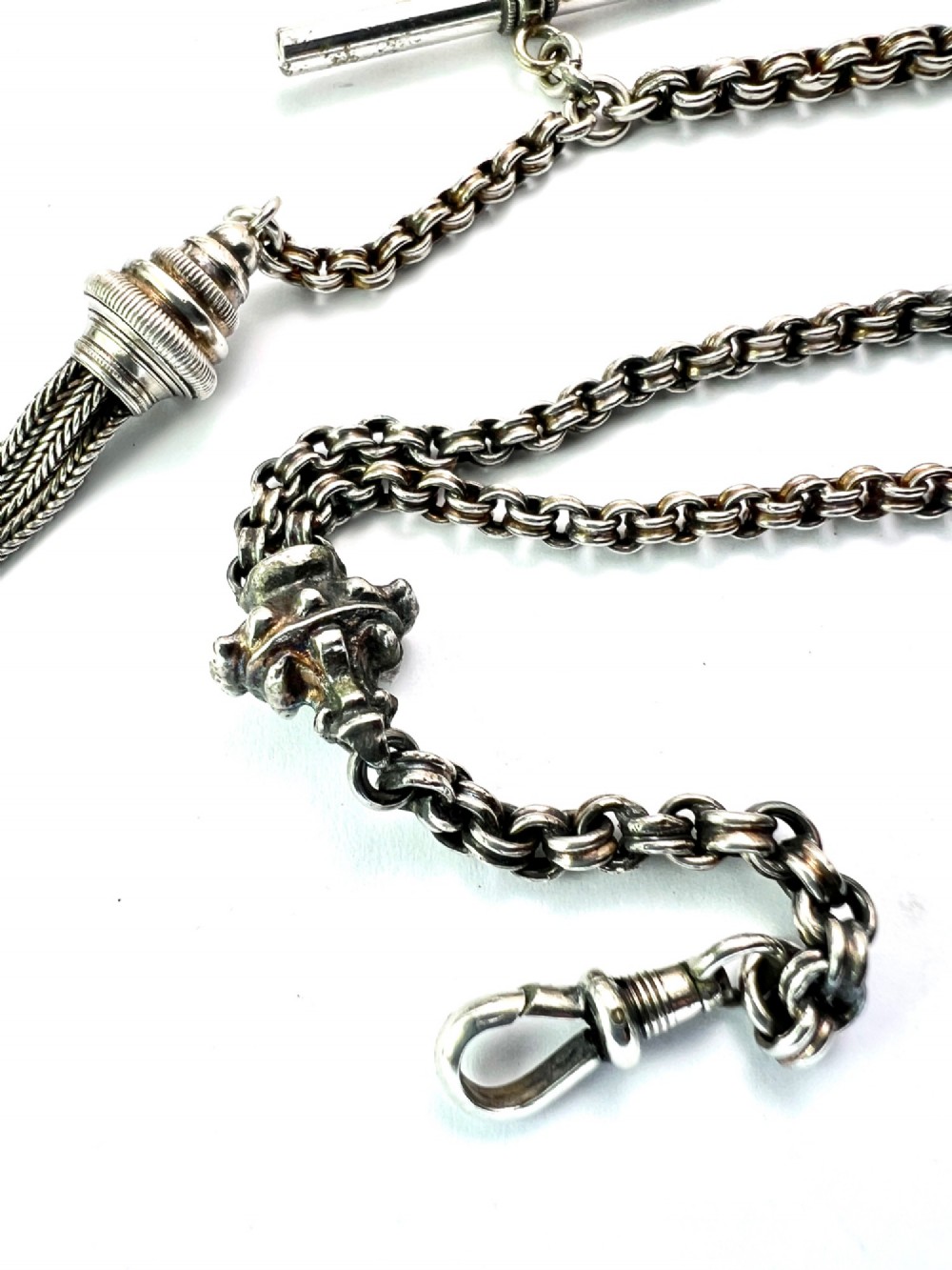 An antique silver Albertina watch chain featuring woven multi-strand links, a T-bar attachment, decorative sliding motifs, a swivel clasp, and a hanging tassel fob. View V