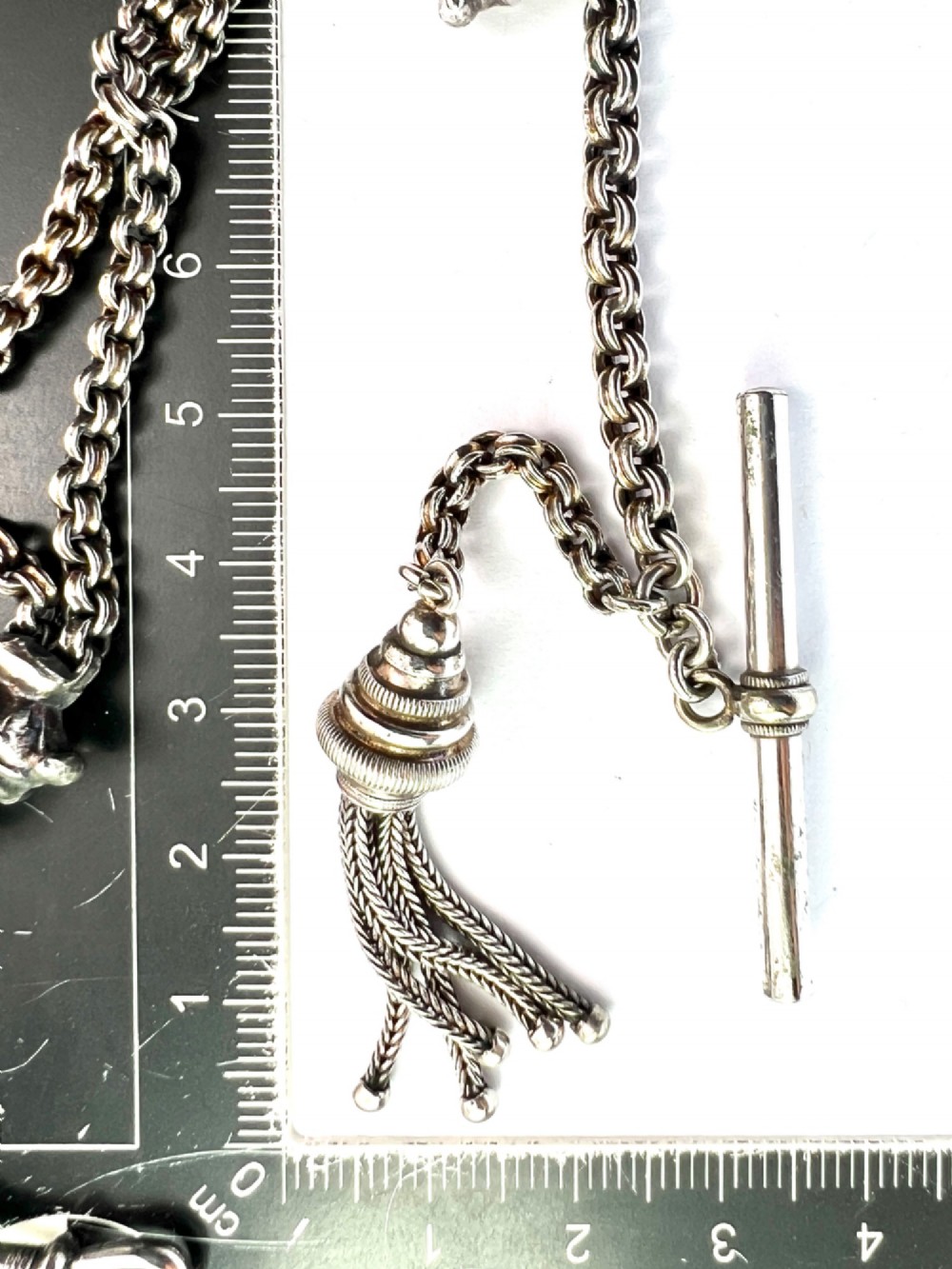 An antique silver Albertina watch chain featuring woven multi-strand links, a T-bar attachment, decorative sliding motifs, a swivel clasp, and a hanging tassel fob. View VI