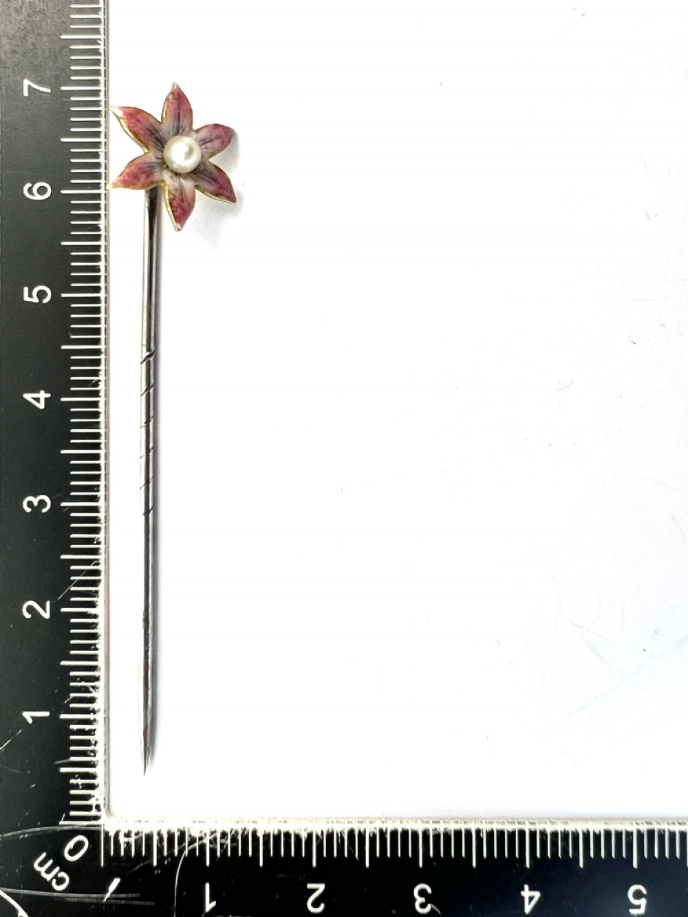 An Art Nouveau stick pin featuring a pink enamelled six-petal flower with a central pearl set on a gold shaft. View VI