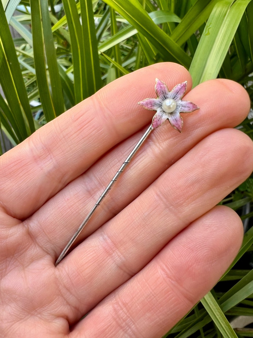 An Art Nouveau stick pin featuring a pink enamelled six-petal flower with a central pearl set on a gold shaft. View VII