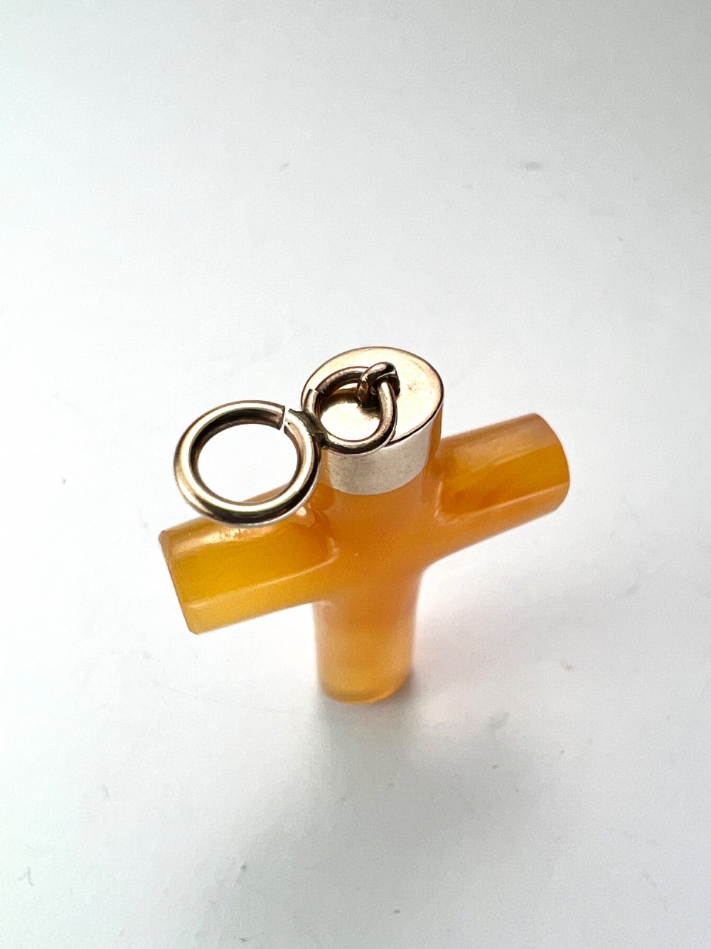 A carved translucent amber agate cross pendant featuring a polished gold cap and suspension bail. View III