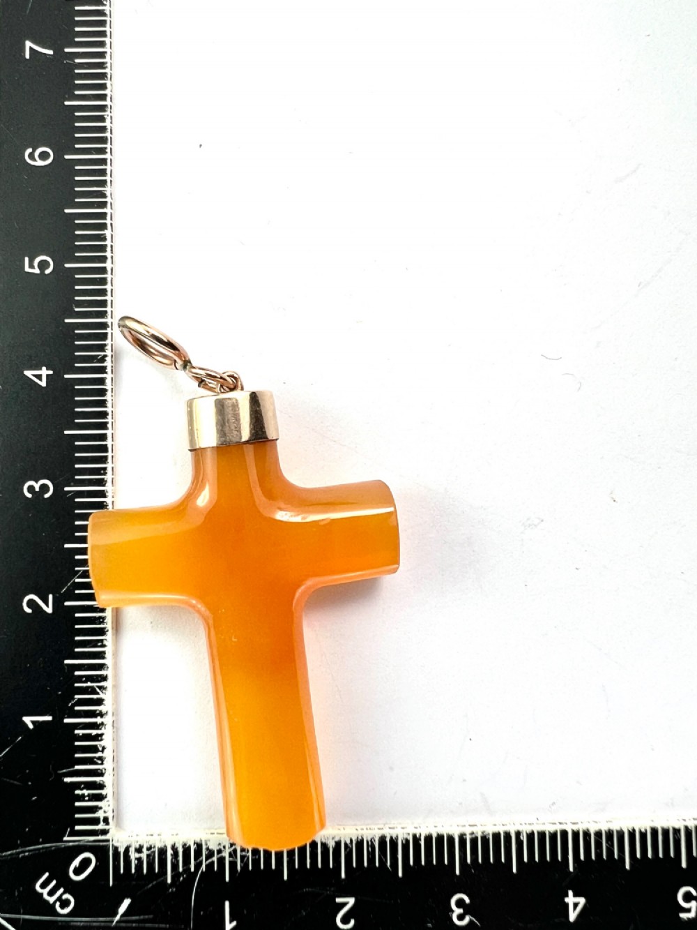 A carved translucent amber agate cross pendant featuring a polished gold cap and suspension bail. View V