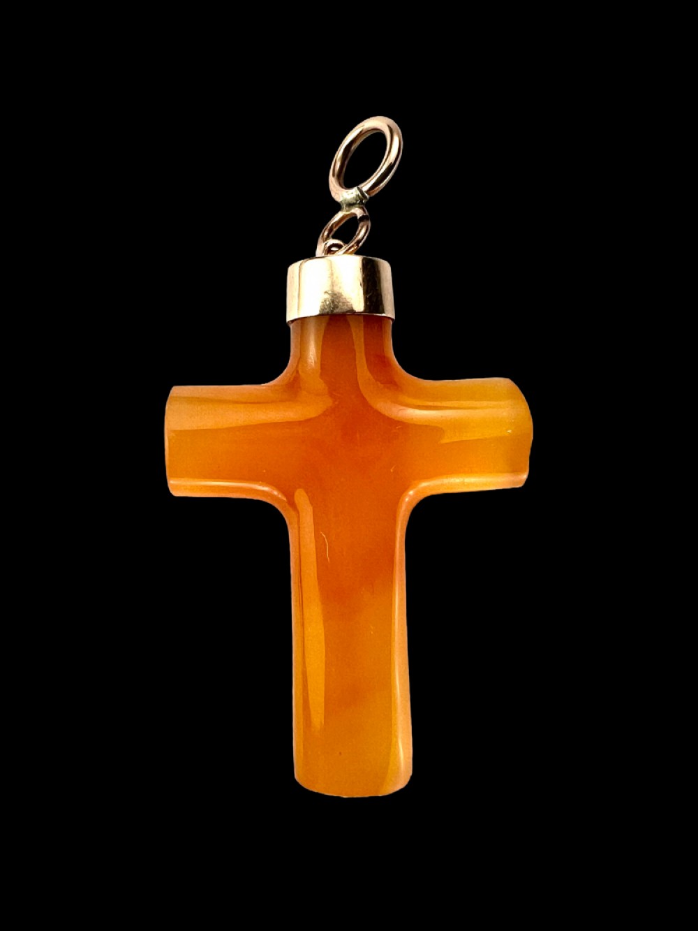 A carved translucent amber agate cross pendant featuring a polished gold cap and suspension bail. View VII