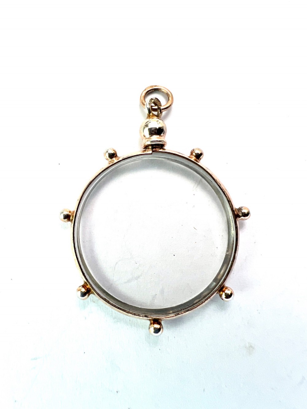 A circular glass locket pendant featuring a gold-toned silver frame with small spherical beads around the outer edge and a threaded top suspension loop. View V