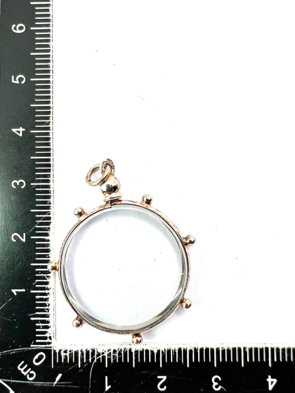 A circular glass locket pendant featuring a gold-toned silver frame with small spherical beads around the outer edge and a threaded top suspension loop. View VI