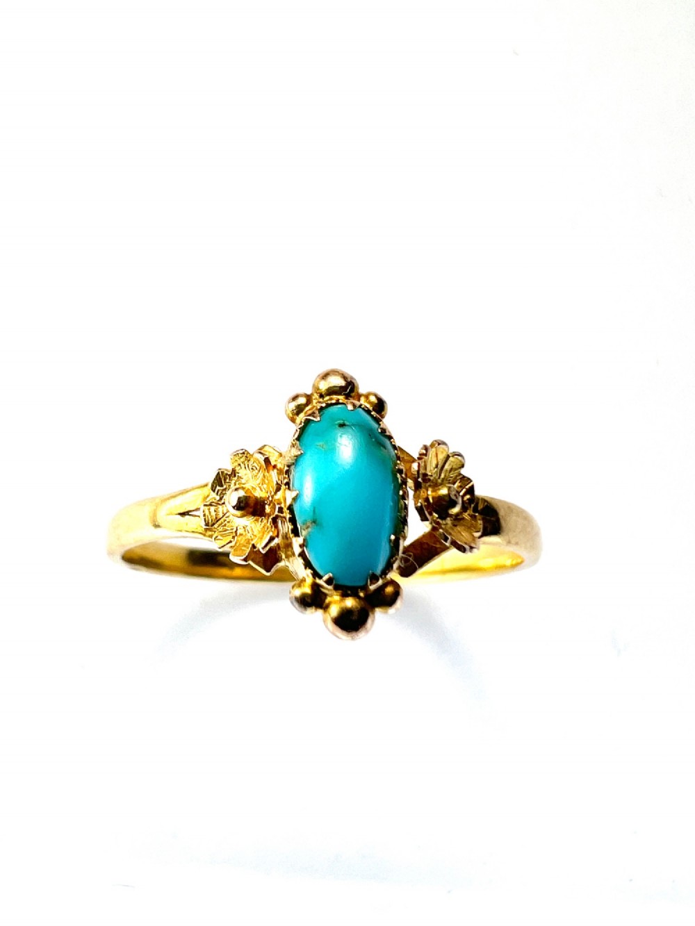 A Victorian 18ct gold ring set with a central oval cabochon turquoise flanked by hand-detailed floral shoulders. View II