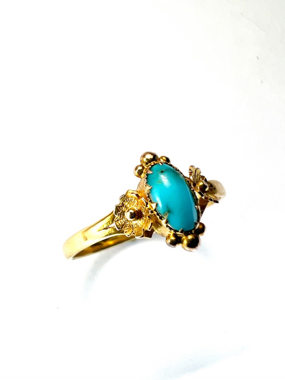A Victorian 18ct gold ring set with a central oval cabochon turquoise flanked by hand-detailed floral shoulders. View III