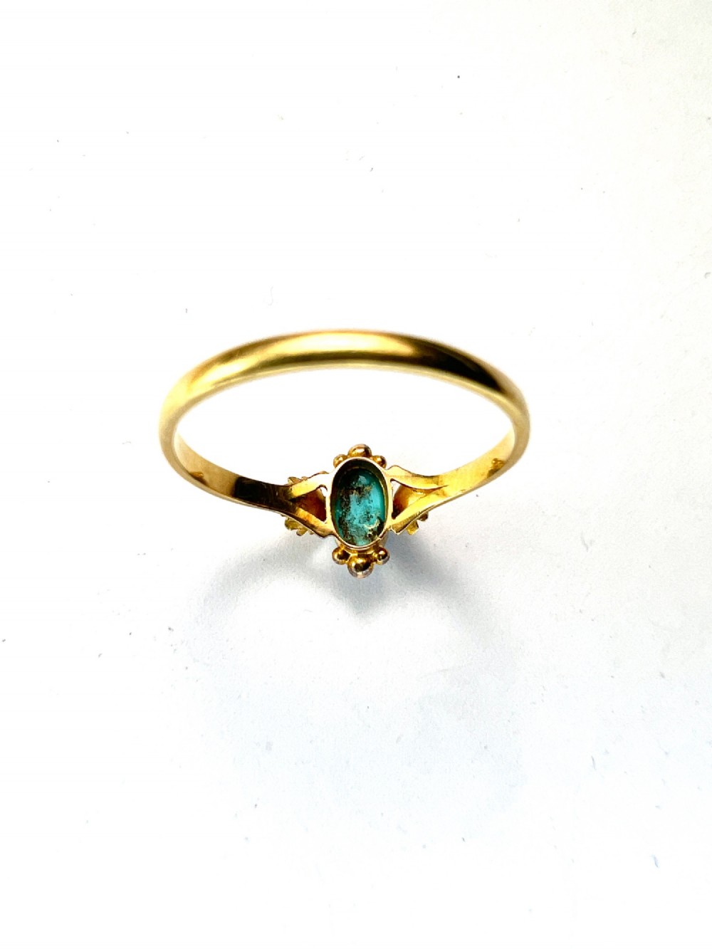 A Victorian 18ct gold ring set with a central oval cabochon turquoise flanked by hand-detailed floral shoulders. View IV