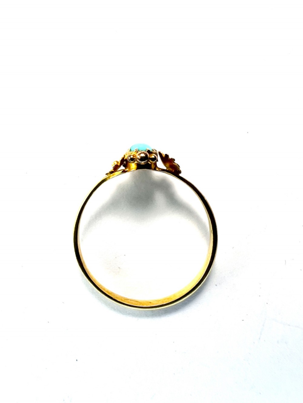 A Victorian 18ct gold ring set with a central oval cabochon turquoise flanked by hand-detailed floral shoulders. View V