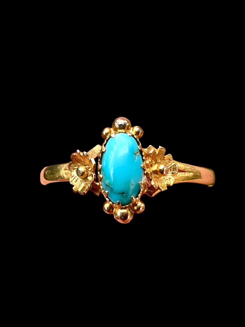 A Victorian 18ct gold ring set with a central oval cabochon turquoise flanked by hand-detailed floral shoulders. View VI