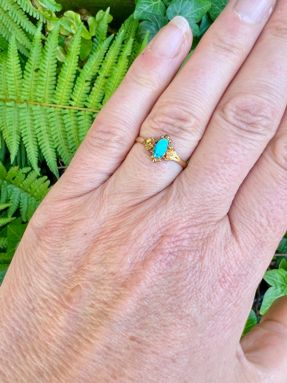 A Victorian 18ct gold ring set with a central oval cabochon turquoise flanked by hand-detailed floral shoulders. View VII