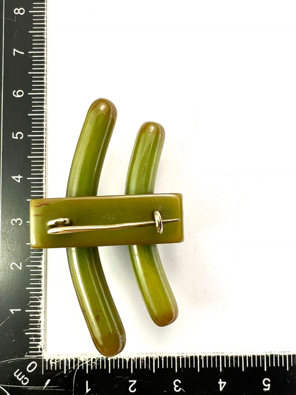 An Art Deco olive green Bakelite brooch featuring curved geometric bars joined by a central band. View VII