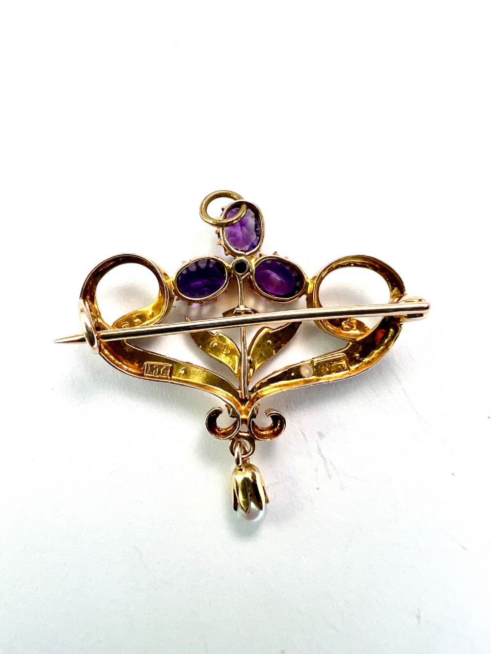 An Edwardian 9ct gold openwork brooch set with three oval-cut purple amethysts, seed pearls along scrolling ribbon motifs, and an articulated pearl drop. View III