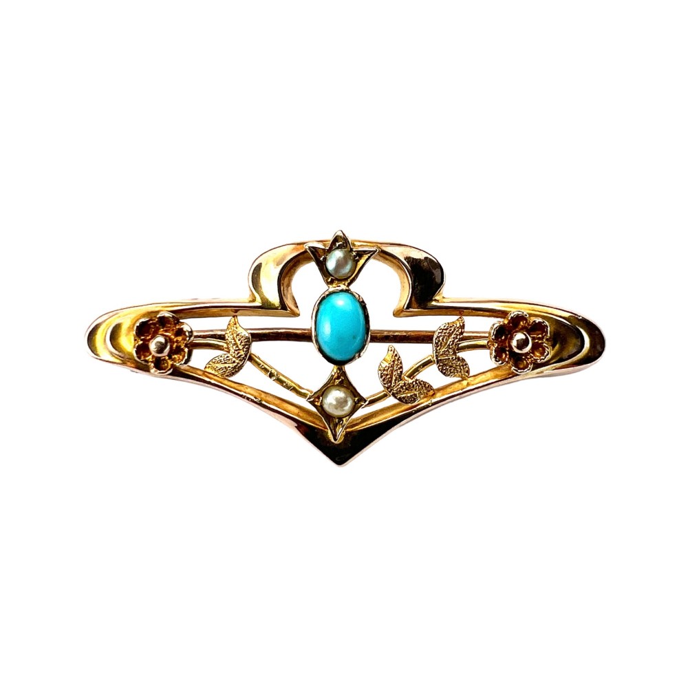 An Edwardian 9ct gold openwork bar brooch featuring a central oval cabochon turquoise flanked by two seed pearls, engraved leaves, and two small gold flowers.