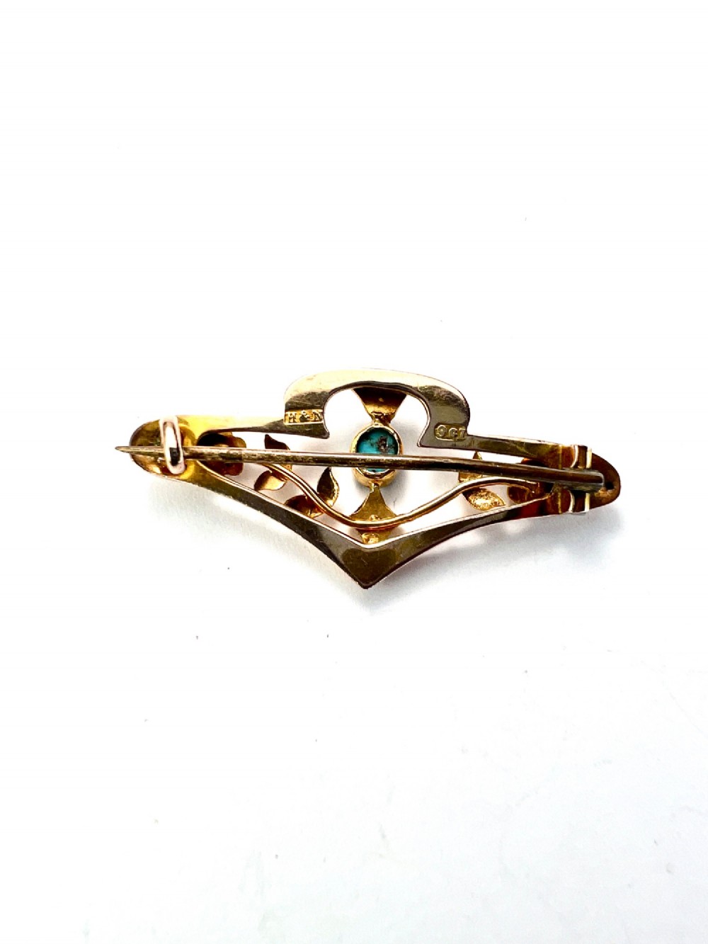 An Edwardian 9ct gold openwork bar brooch featuring a central oval cabochon turquoise flanked by two seed pearls, engraved leaves, and two small gold flowers. View II