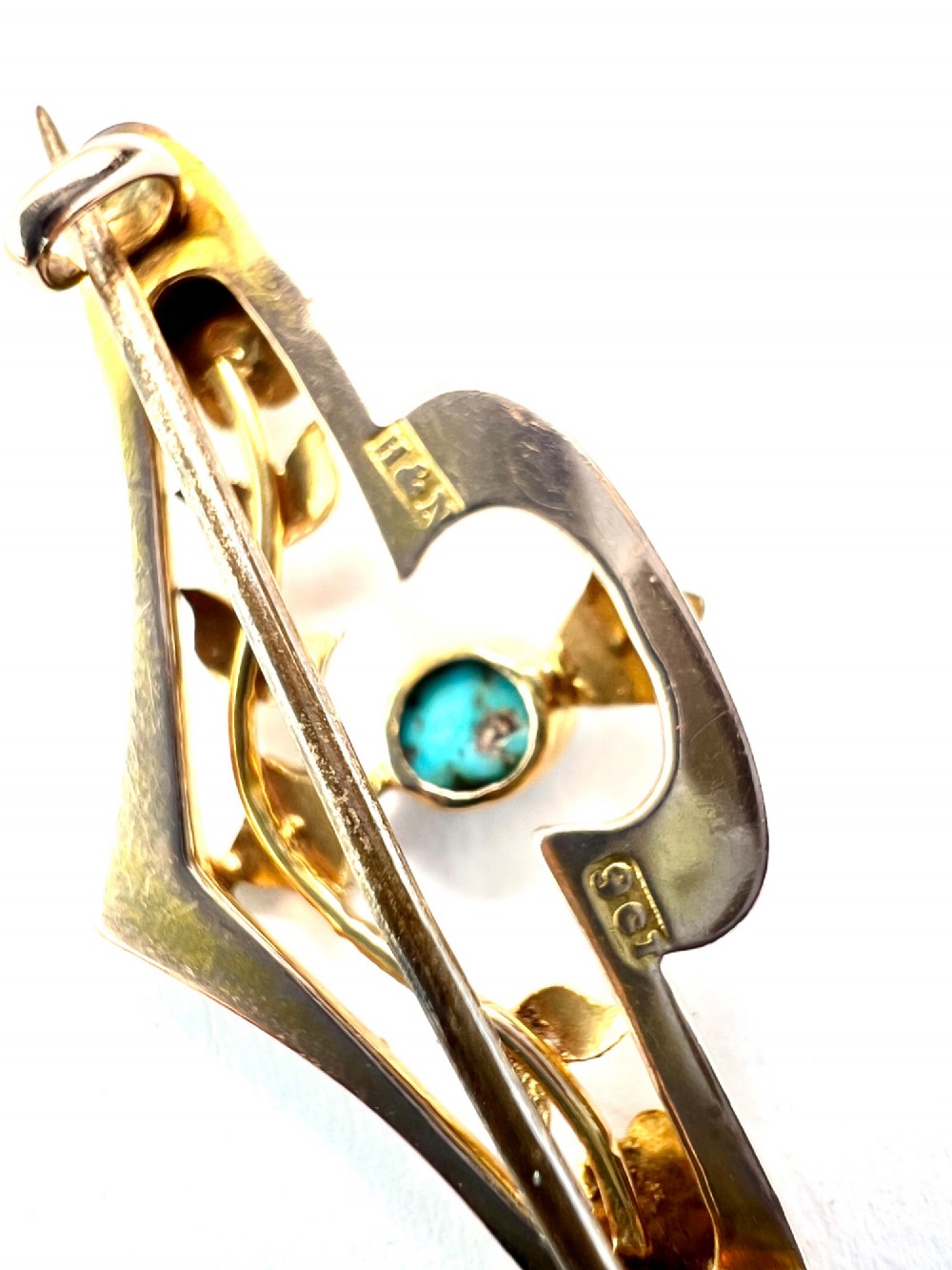 An Edwardian 9ct gold openwork bar brooch featuring a central oval cabochon turquoise flanked by two seed pearls, engraved leaves, and two small gold flowers. View III