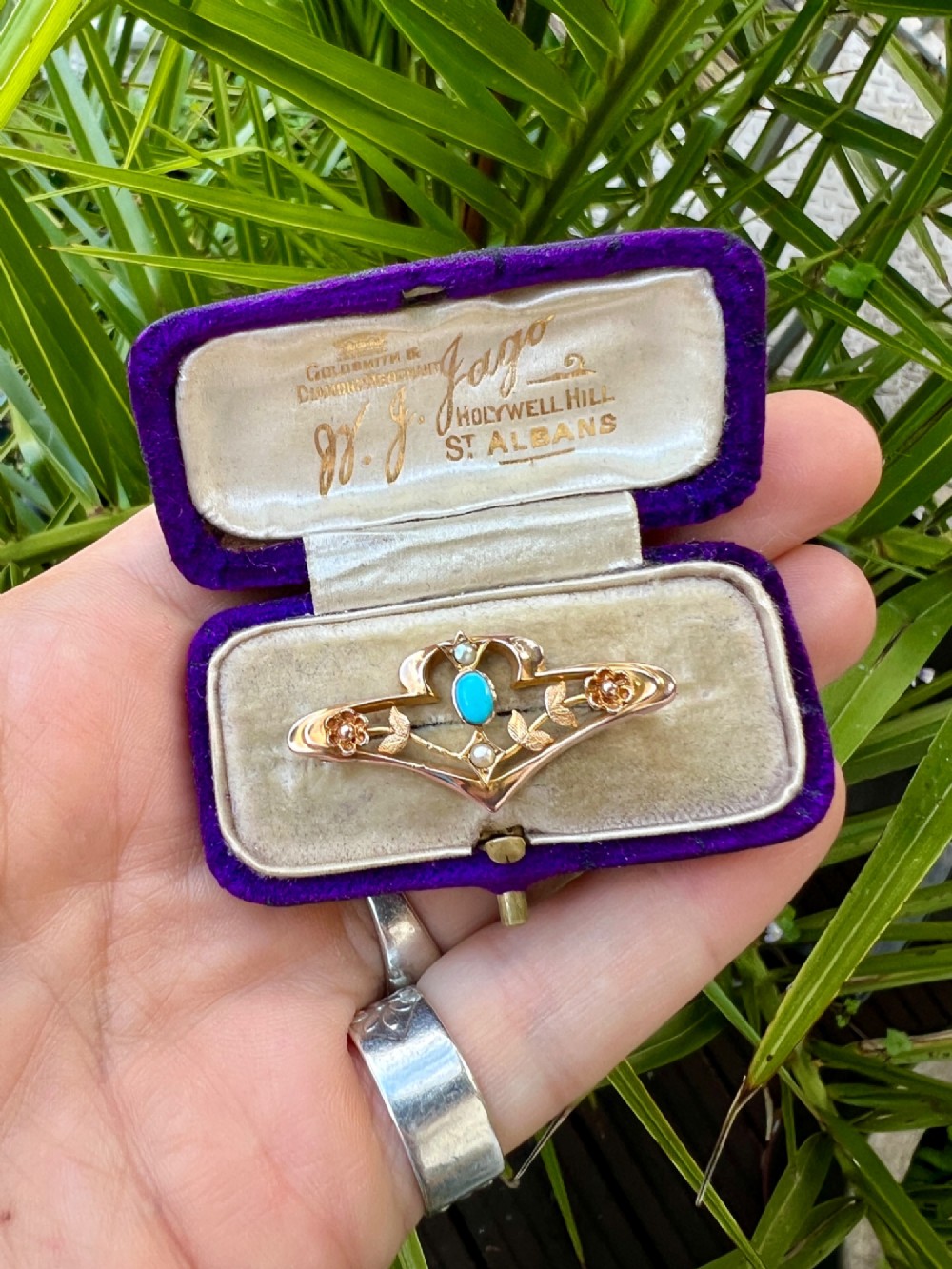 An Edwardian 9ct gold openwork bar brooch featuring a central oval cabochon turquoise flanked by two seed pearls, engraved leaves, and two small gold flowers. View V