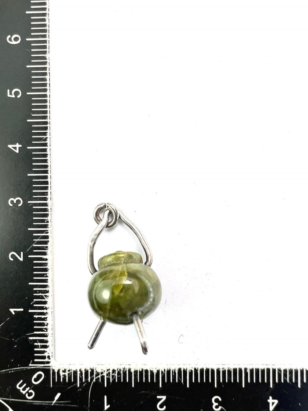 An Edwardian sterling silver and carved green stone cauldron pendant featuring tripod feet, a moveable silver handle, and hallmarked stamp details. View V