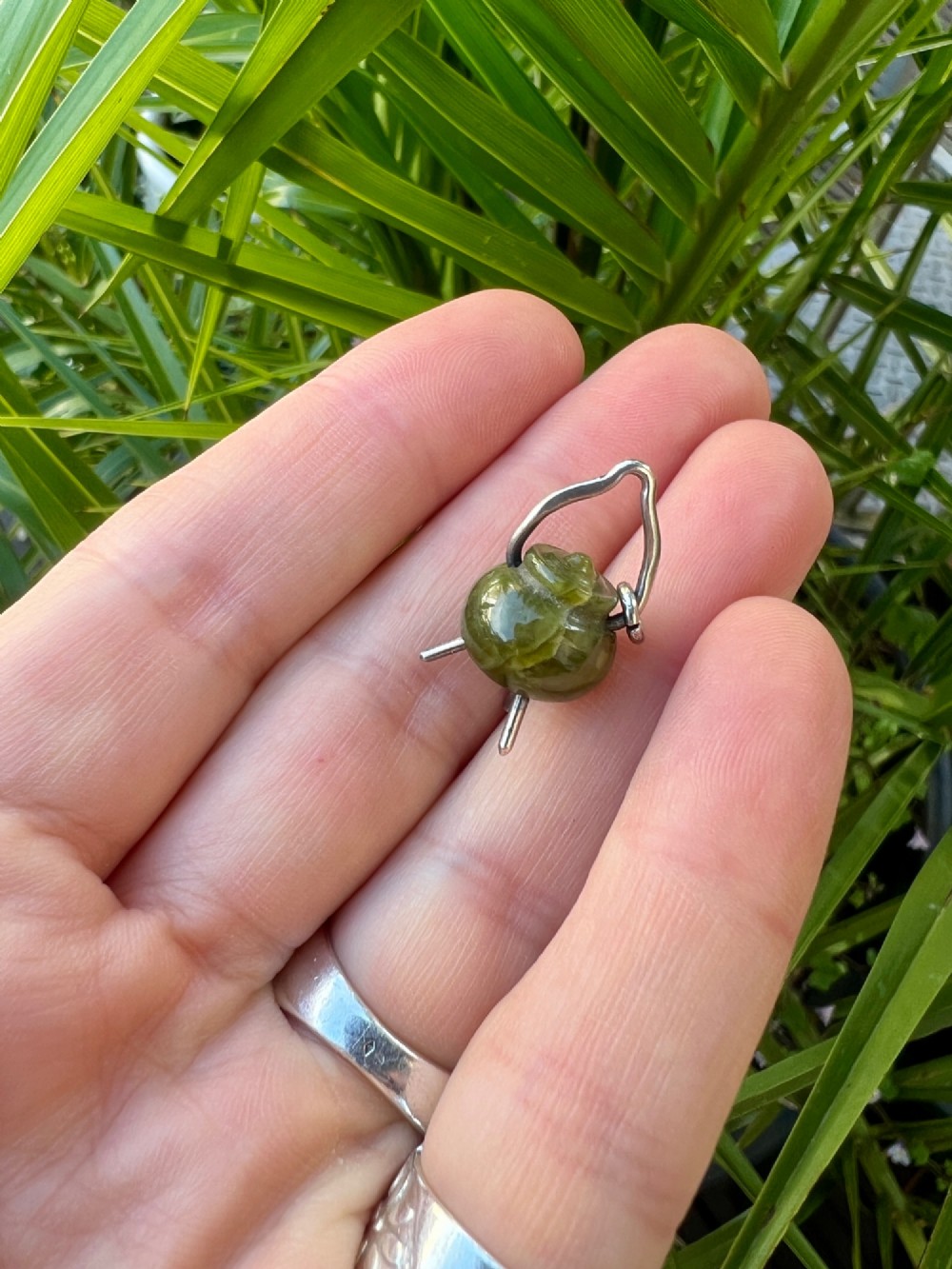 An Edwardian sterling silver and carved green stone cauldron pendant featuring tripod feet, a moveable silver handle, and hallmarked stamp details. View VI