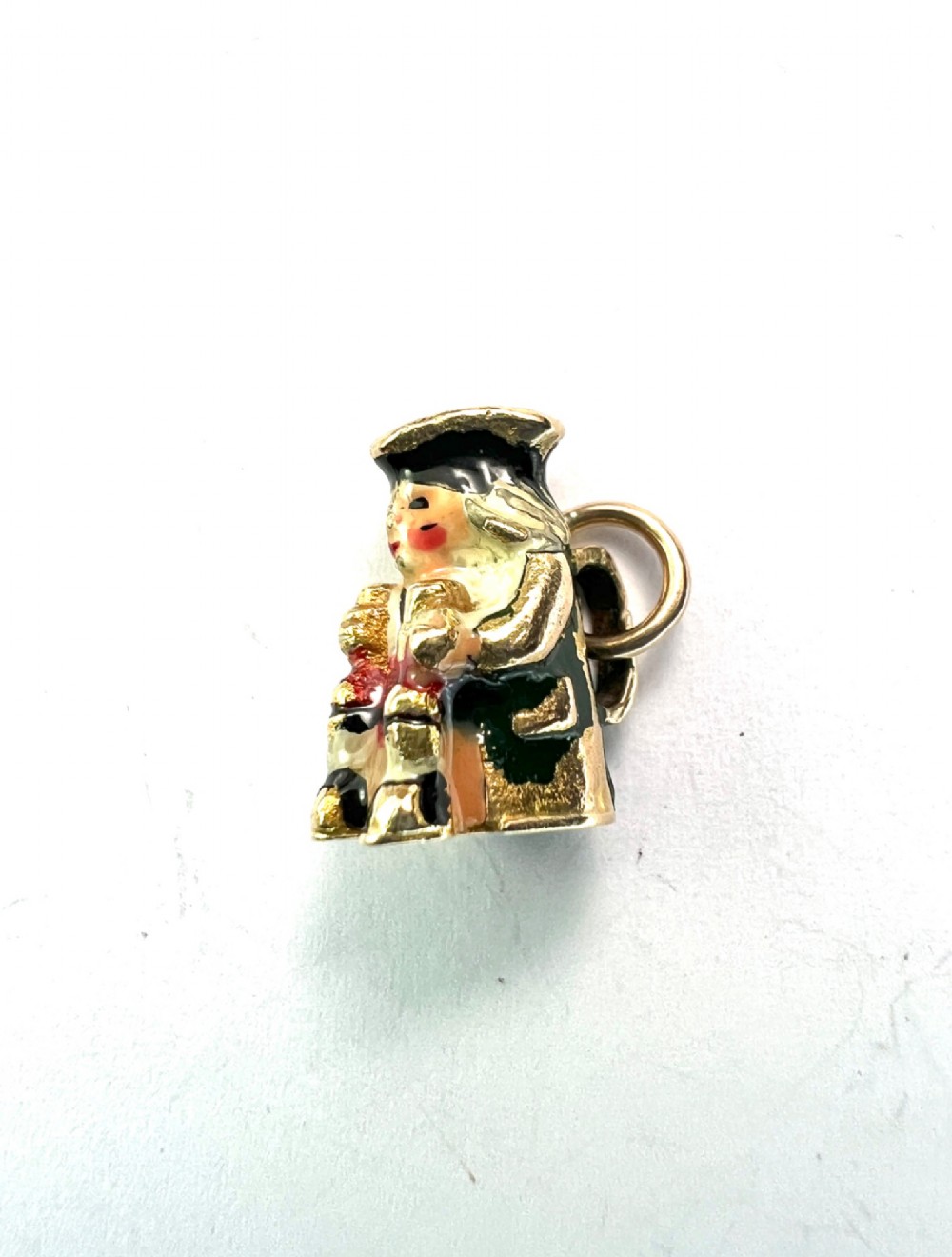 A miniature 9ct gold and enamel Toby jug charm depicting a seated figure in a tricorn hat with red and black painted details. View V