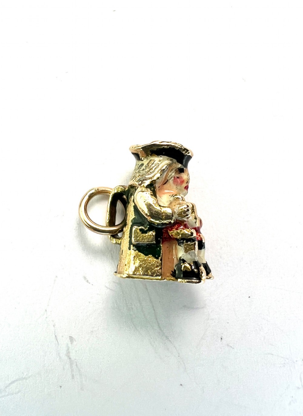 A miniature 9ct gold and enamel Toby jug charm depicting a seated figure in a tricorn hat with red and black painted details. View VI