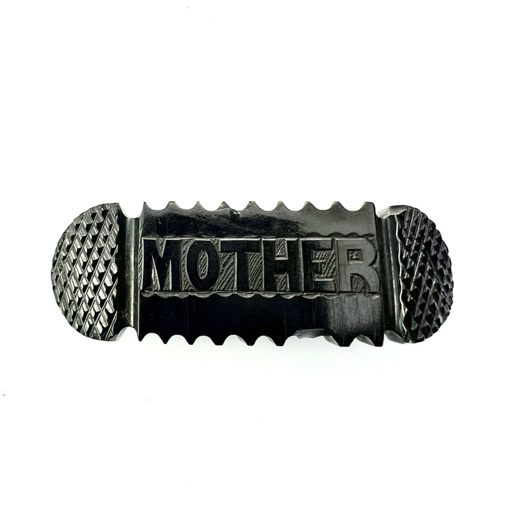 An oblong carved black Whitby jet brooch featuring the raised carved word MOTHER flanked by cross-hatched ends and notched borders.