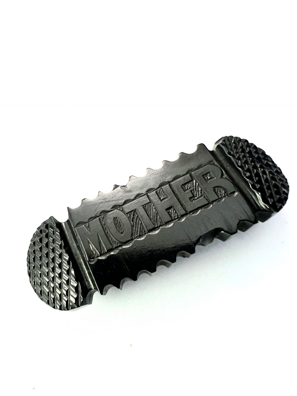 An oblong carved black Whitby jet brooch featuring the raised carved word MOTHER flanked by cross-hatched ends and notched borders. View II