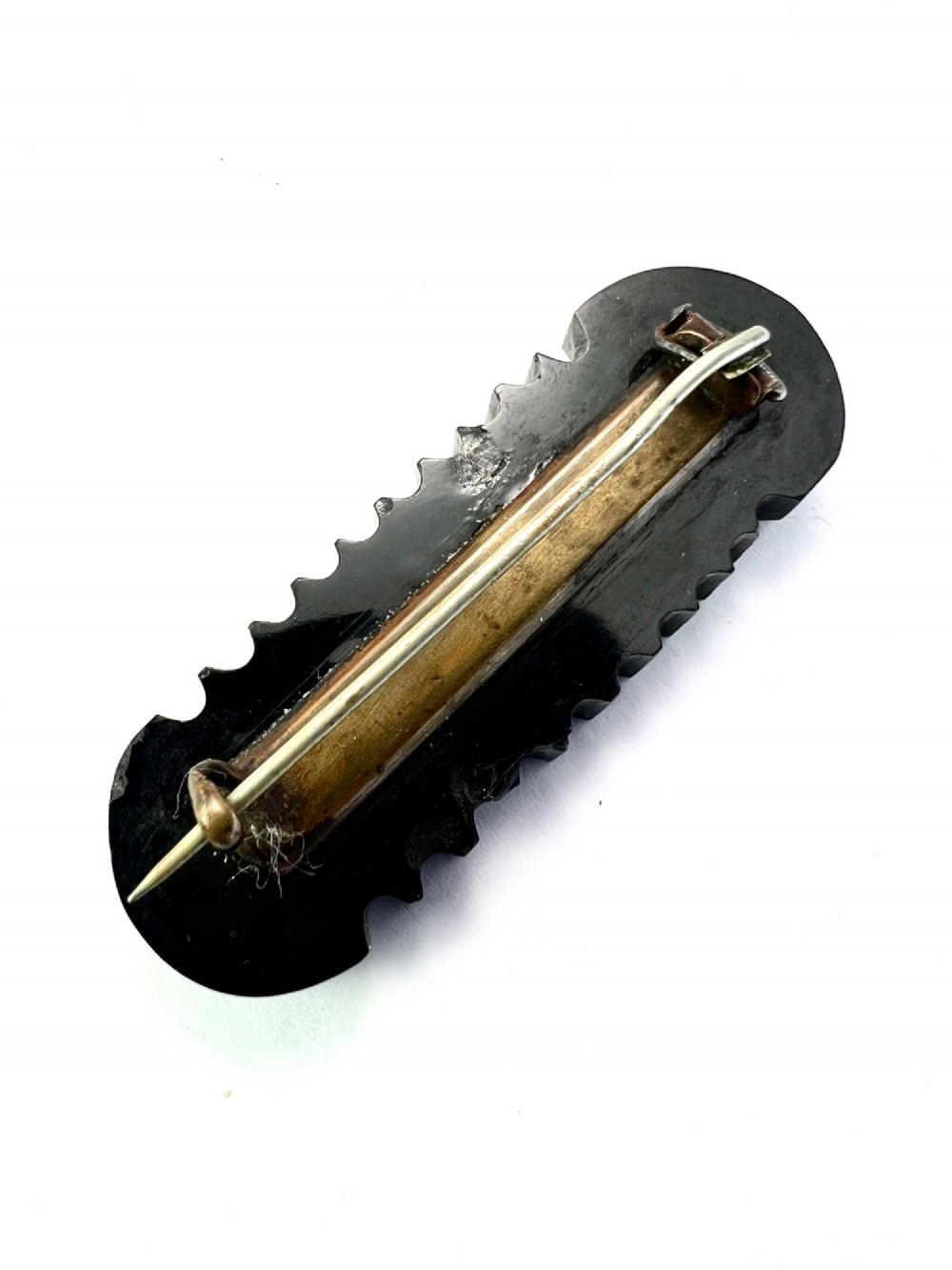 An oblong carved black Whitby jet brooch featuring the raised carved word MOTHER flanked by cross-hatched ends and notched borders. View IV