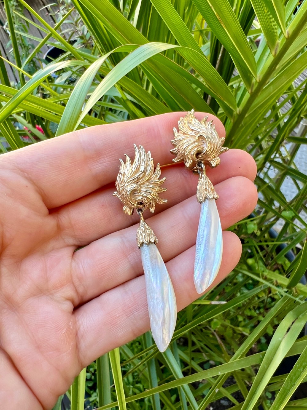 A pair of vintage gold-tone clip-on earrings featuring textured flame-like tops and hanging elongated mother-of-pearl drop pendants. View V