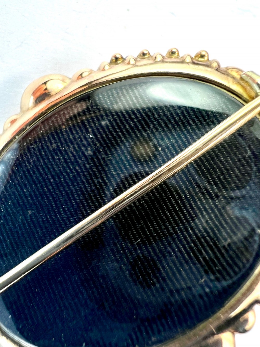 An ornate oval Victorian Etruscan Revival gold brooch featuring a central oval-cut deep red garnet surrounded by detailed relief metalwork and beaded borders. View VI