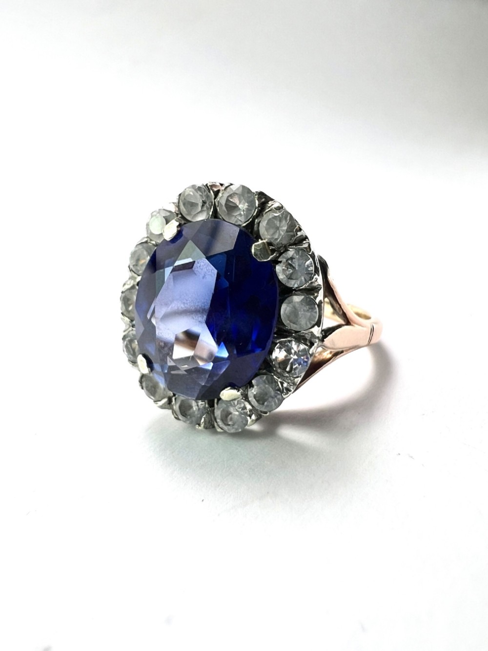An Edwardian sapphire halo ring featuring a large oval blue sapphire encircled by a halo of clear accent stones set in silver with a yellow gold shank. View III