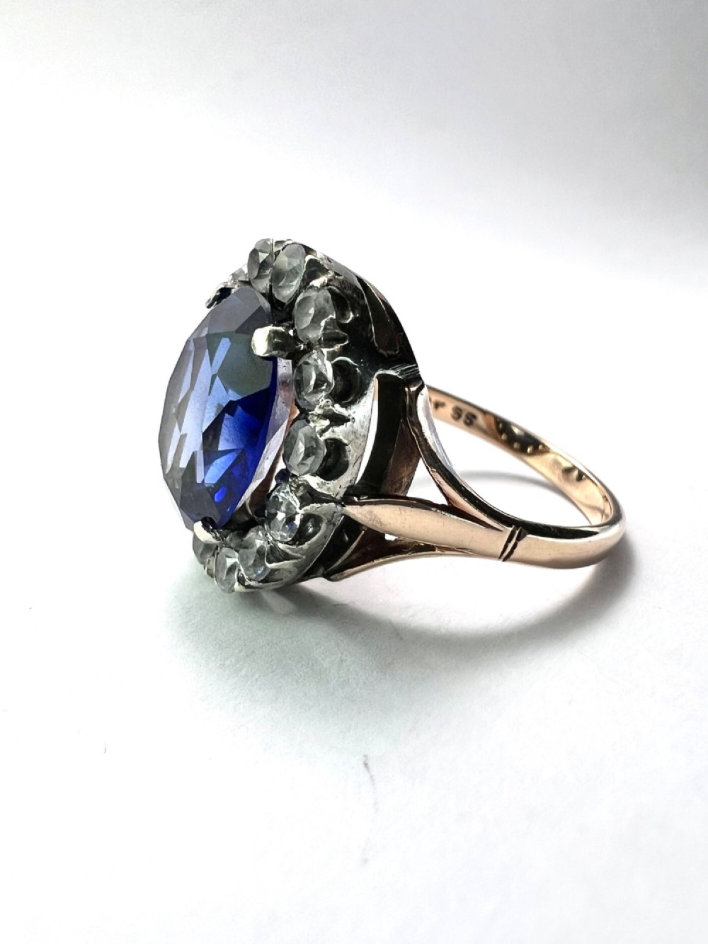 An Edwardian sapphire halo ring featuring a large oval blue sapphire encircled by a halo of clear accent stones set in silver with a yellow gold shank. View IV