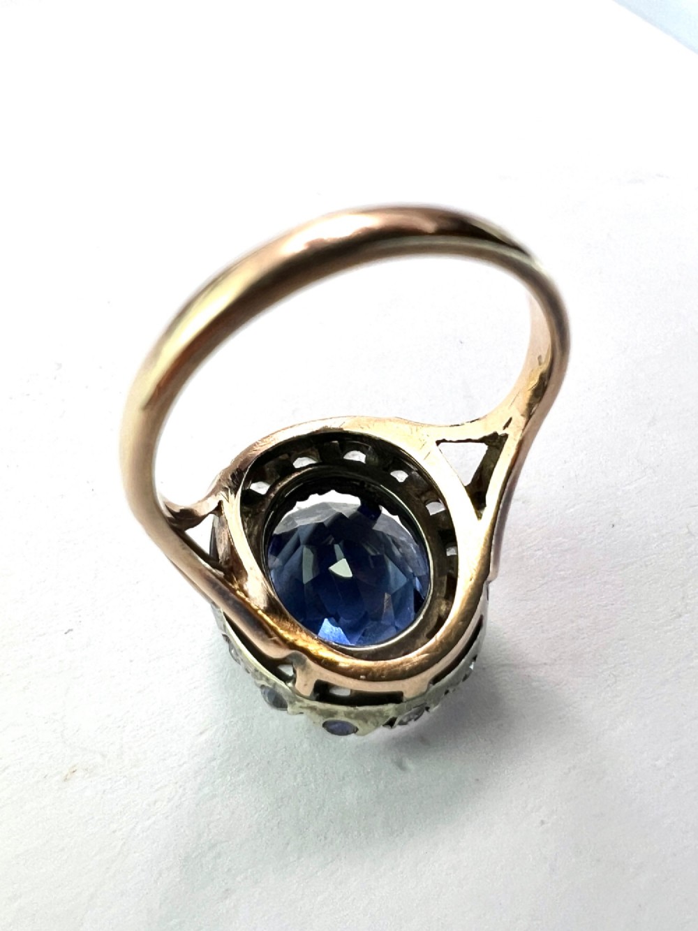 An Edwardian sapphire halo ring featuring a large oval blue sapphire encircled by a halo of clear accent stones set in silver with a yellow gold shank. View VI