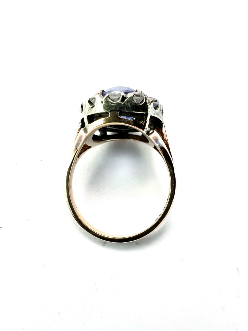 An Edwardian sapphire halo ring featuring a large oval blue sapphire encircled by a halo of clear accent stones set in silver with a yellow gold shank. View VII