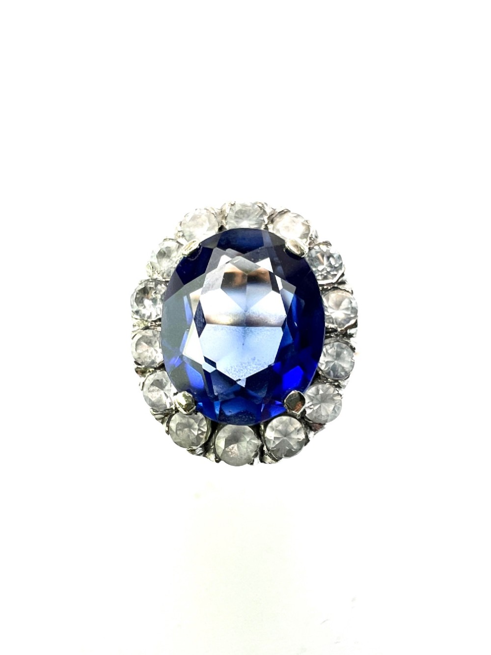 An Edwardian sapphire halo ring featuring a large oval blue sapphire encircled by a halo of clear accent stones set in silver with a yellow gold shank. View VIII