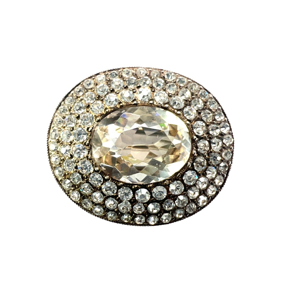 An oval Edwardian brooch featuring a large central oval paste stone bordered by multiple rows of smaller brilliant-cut paste stones in a silver mounting.